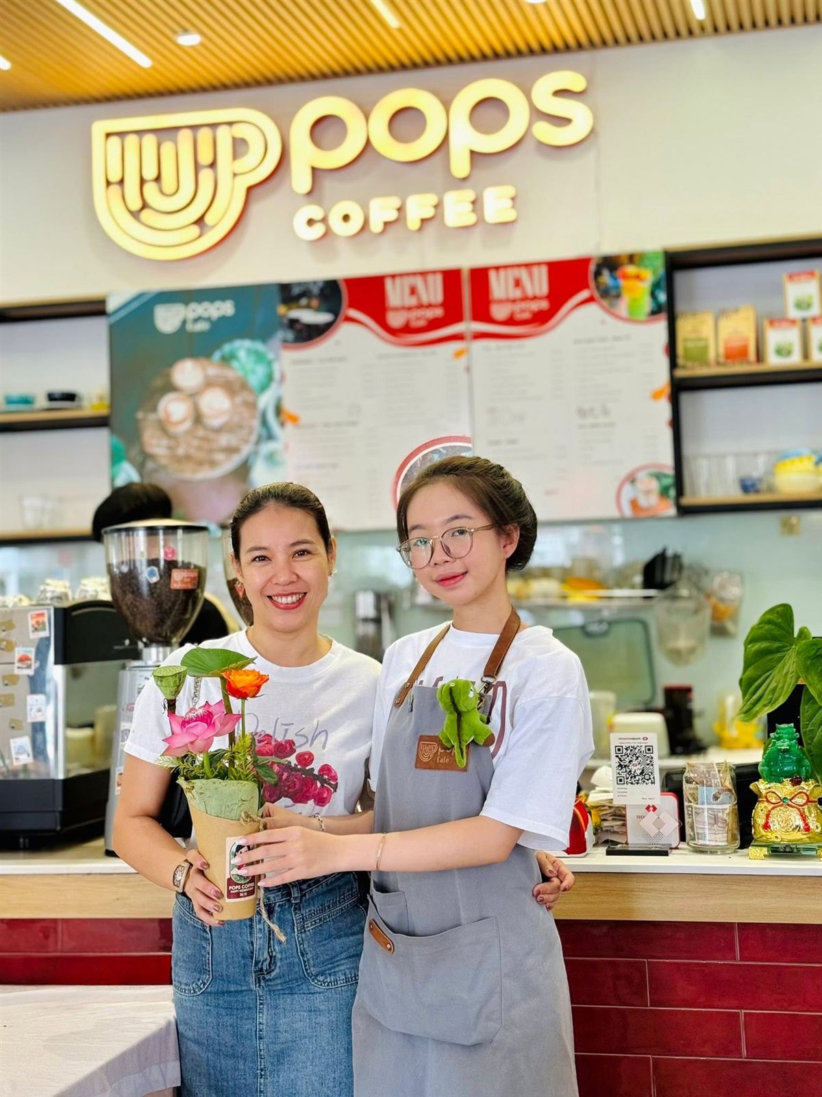 Hai nhân viên cầm bó hoa tươi trước quầy POPS Coffee