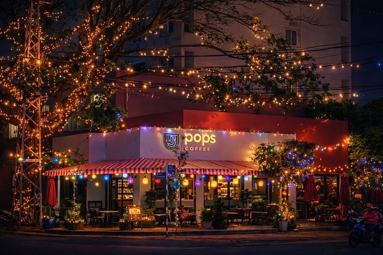 Mặt tiền POPS Coffee lúc chập tối, hàng cây và mái hiên giăng đèn vàng